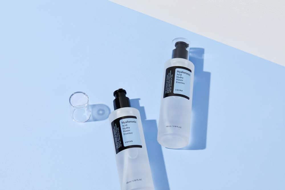COSRX:s Hyaluronic Acid Hydra Power Essence 100ml offre des avantages hydratants sur une surface bleue.