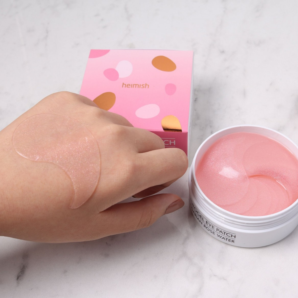 Une main tenant un rose Bulgarian Rose Hydrogel Eye Patch 60st de heimish et applique un masque pour les yeux.